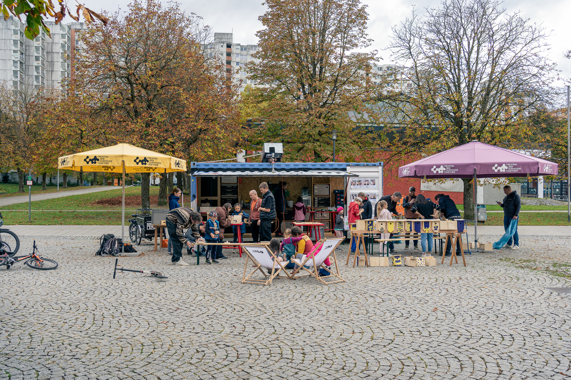 Anischt des kleinen MakerSpaces am Theodor-Heuss-Platz. Der MakerSpace besteht aus einem umgebauten Seecontainer. Das Foto zeigt Menschen, die am Workshop zum Bau von Nistkästen teilnehmen. 