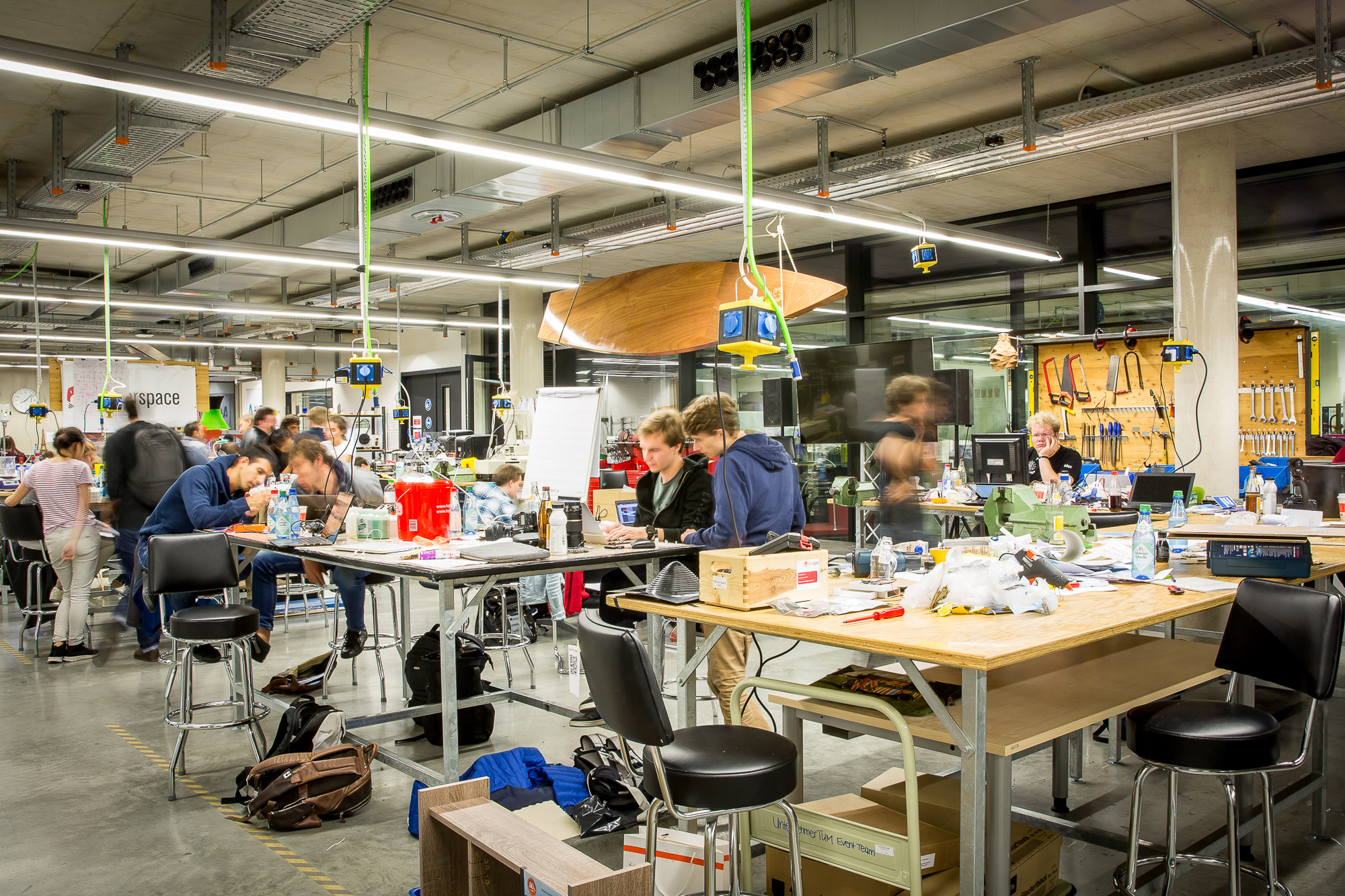 Foto einer Werkstatt im MakerSpace München. Es sind Menschen zu sehen, die an Tischen und Werkbänken handwerklich arbeiten. 