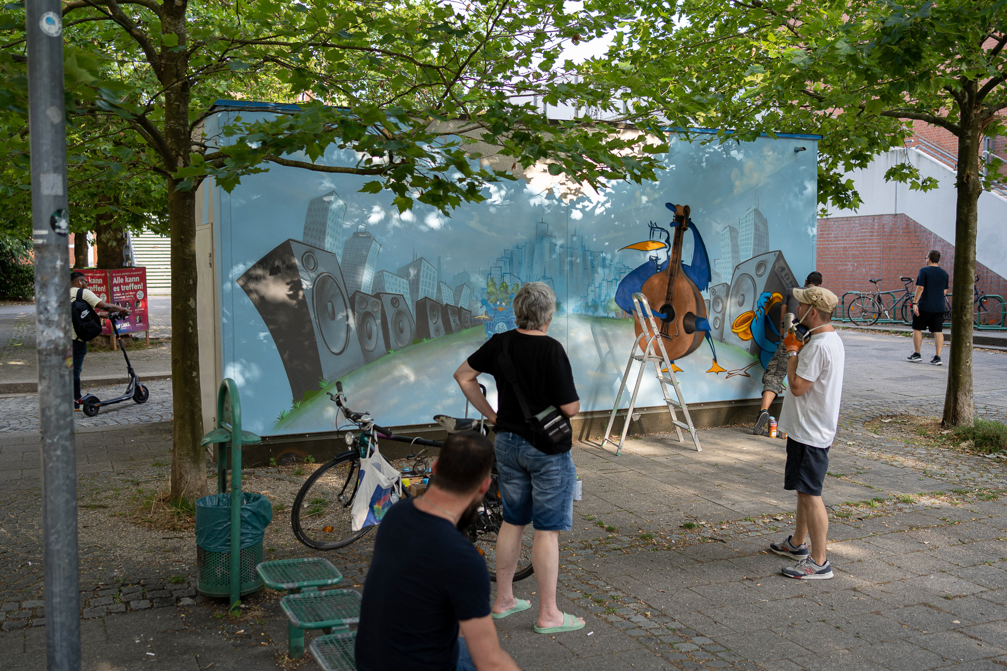 Foto der Künstler*innen während des Bemalens des Beton-Quaders am Platz zwischen PEP und Wohnring. 